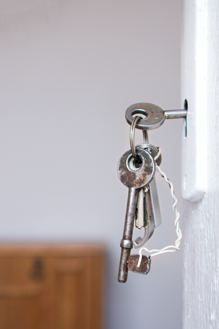 about-us Close-up of vintage keys in a door keyhole with rustic metal and wood textures.
