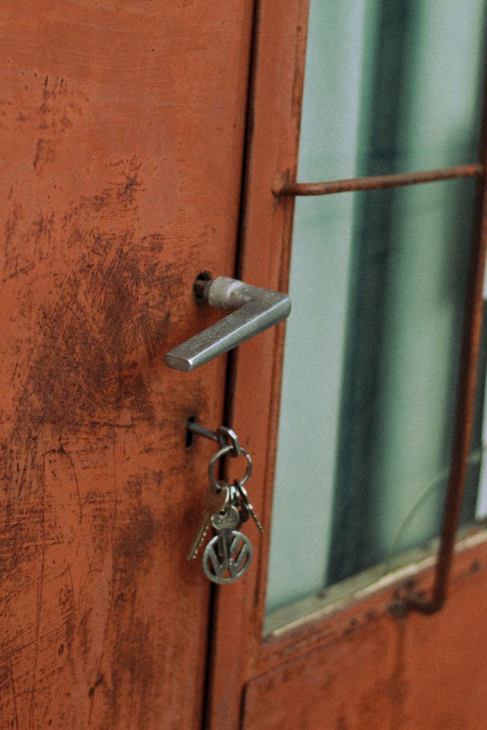 Close-up of a rustic red door handle with a vintage keychain dangling from the lock.