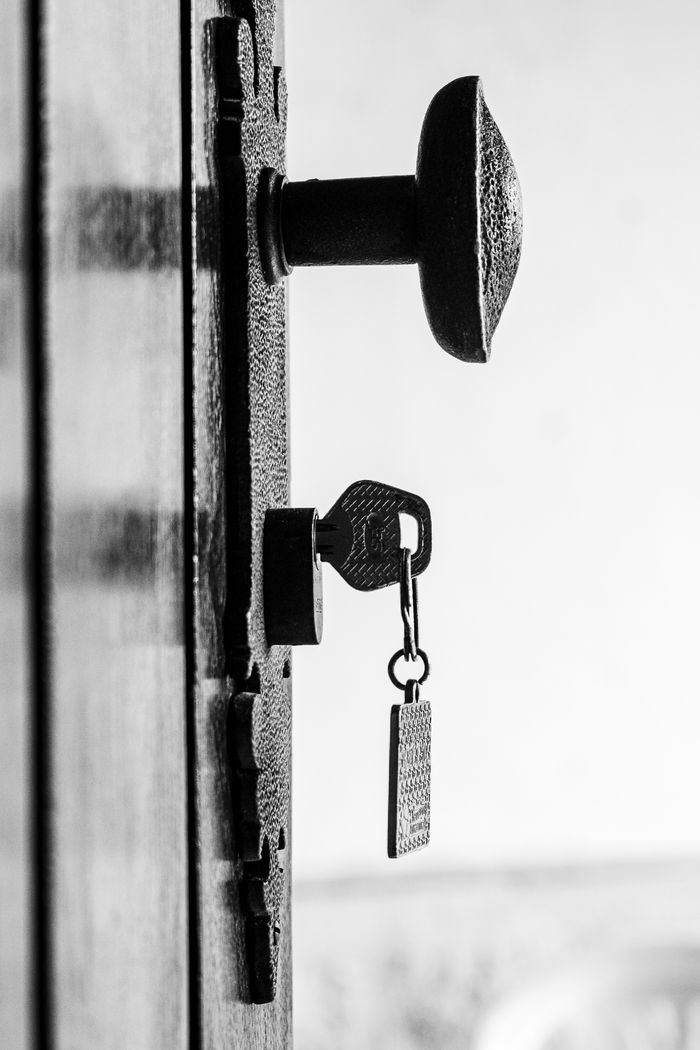 our-story Close-up of a key in an antique lock on a rustic door, black and white.