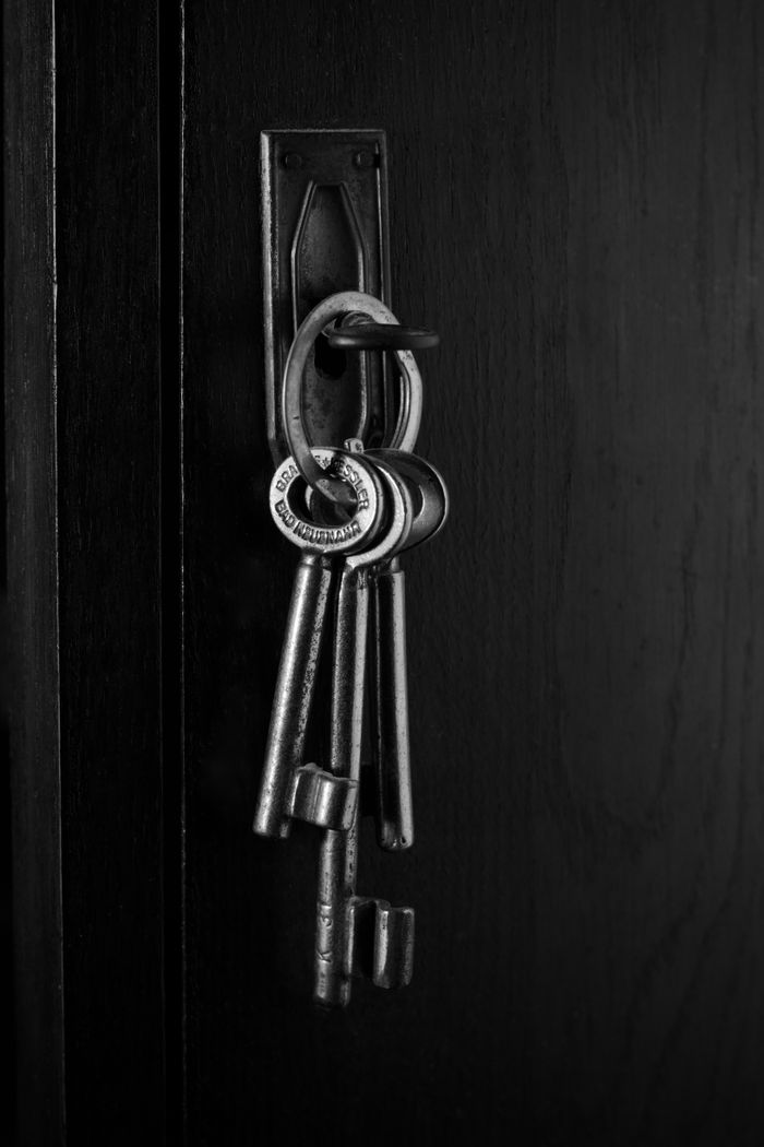 Monochrome image of vintage skeleton keys hanging from a dark wood door, evoking mystery.